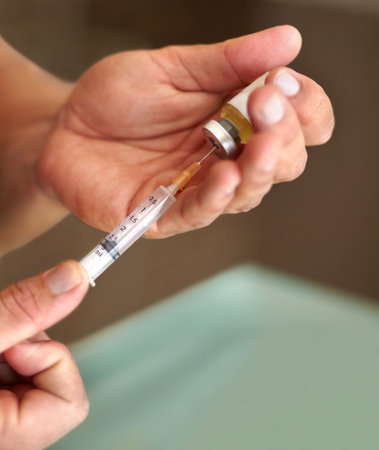 Preparing to inject. Closeup of a man filling a syringe with a clear liquid.