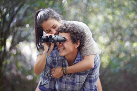 Here have a look. A young man giving his girlfriend a piggyback while she holds bincoulars.の写真素材