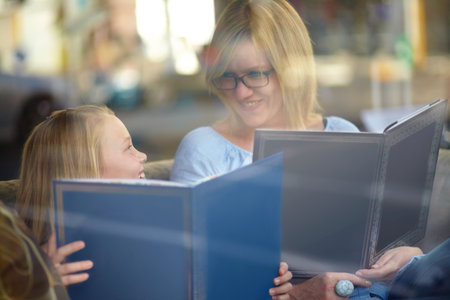 Reading together. A young blonde girl sitting next to her mother while they both read.の写真素材