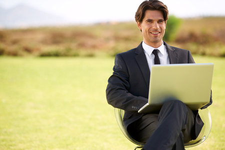 Modern technology makes a truly mobile office possible. Portrait of a young businessman sitting outside with his laptop.の写真素材