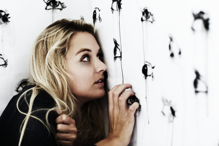 Theyre everywhere...Studio shot of a paranoid young woman looking at painted eyes on a wall.
