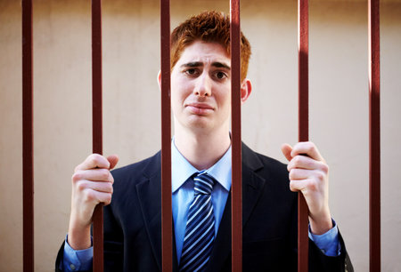 Bad business has its consequences. An unhappy businessman behind bars.の写真素材