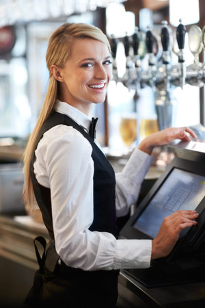 Thank you for coming. Beautiful barmaid smiling as she waits on a customer for payment.