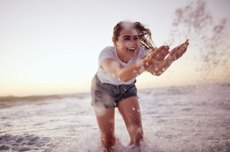 Splash, ocean and woman at the beach in the water, enjoying the waves at sunset. Summer adventure, holiday and happy girl having fun on vacation. Freedom, joy and playful female splashing in the seaの写真素材