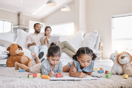 Little two girls drawing with colouring pencils lying on living room floor with their parents relaxing on couch. Little children sisters siblings colouring in during family time at homeの写真素材