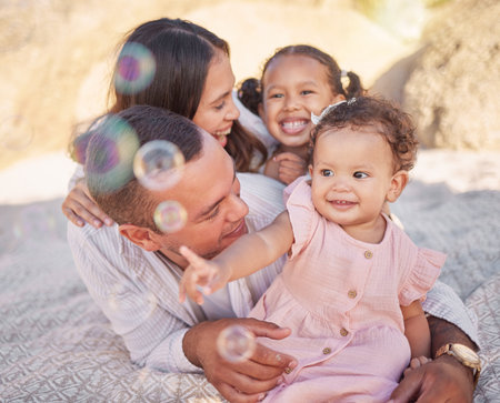 A happy mixed race family of four enjoying fresh air at the beach. Hispanic couple bonding with their daughters while having a picnic in a garden or parkの写真素材