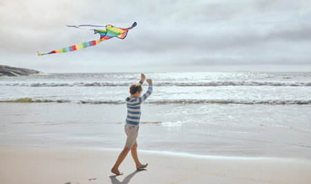 One little caucasian boy flying a colourful rainbow kite in the wind at the beach. Playful young child having fun outdoors. The innocence of childhoodの写真素材