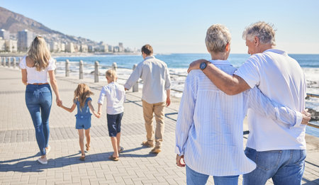 Rear view of a senior couple strolling on a seaside promenade while their children and grandchildren...
