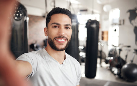Portrait of one confident young hispanic man taking selfies while exercising in a gym. Happy mixed race guy smiling while working as a trainer and instructor in a fitness centreの写真素材