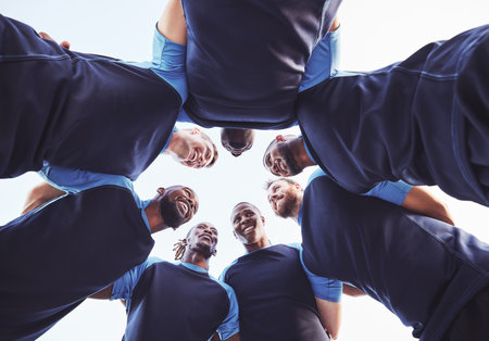 Below diverse group of rugby players standing in a huddle together outside on a field. Young male athletes looking serious and focused while huddled together as a team. Ready for a tough gameの写真素材