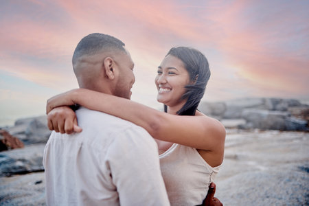 Closeup of an young affectionate mixed race couple standing on the beach and smiling during sunset outdoors. Hispanic couple showing love and affection on a romantic date at the beachの写真素材
