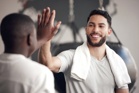 One confident young hispanic man giving a high five to his friend while exercising in a gym. Happy mixed race guy staying motivated while celebrating the end of a successful training workout with anの写真素材