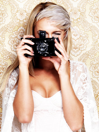 The eye of the glamorous beholder. A glamourous young woman in retro attire holding a camera while posing against a paisley background.の写真素材