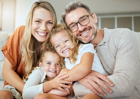 Portrait of a happy Caucasian family of four relaxing in the living room at home. Loving smiling family being affectionate together. Young couple bonding with their little kids at homeの写真素材