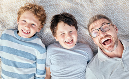 Carefree loving father from above relaxing with his cute little playful sons. Happy caucasian family bonding together. Cheerful kids spending quality time with single dadの写真素材