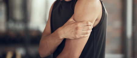 Hands of a bodybuilder with arm pain. Fit man with a sore bicep cropped. Active athlete touching their sore arm in the gym. Athlete with a hurt arm injury in the gym. Fit man with a physical problemの写真素材