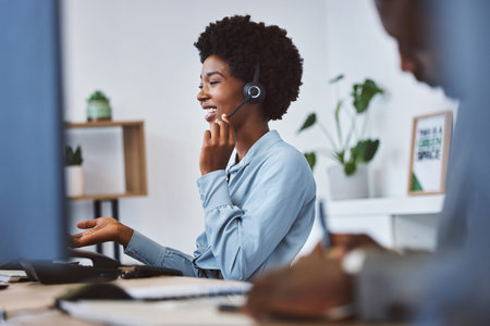 Happy young african american call centre telemarketing agent talking on a headset while working on...