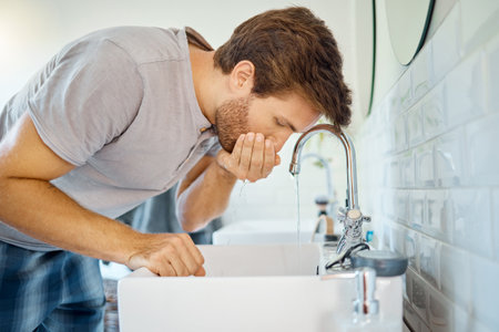 One handsome man rinsing his mouth in a bathroom at home. Caucasian male using mouthwash for fresh breath in his apartmentの写真素材