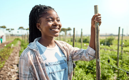 Happy farmer standing in her garden. African american farmer thinking on her farm. Happy farmer working on her farm. Farm worker looking away. Farmer looking at her produce on the farm.の写真素材