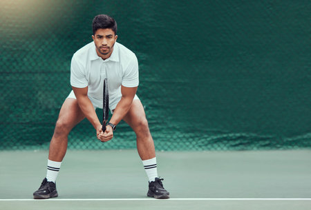 Full length indian tennis player holding a racket and ready to play game on court. Serious and focused ethnic athlete alone in stance. Playing competitive match to stay fit and healthy in sports clubの写真素材