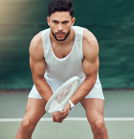 Portrait of mixed race tennis player holding racket and ready to play court game. Serious and focused hispanic athlete alone in stance. Playing competitive match to stay fit and healthy in sports cluの写真素材