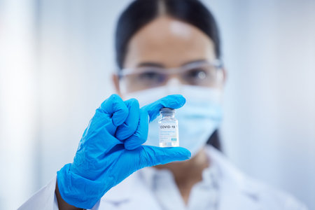 Covid, innovation and woman scientist with the vaccine or virus cure in a medical laboratory after research analysis. Face mask, safety and healthcare science doctor holding antivirus medicineの写真素材