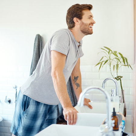 One handsome man checking his teeth in a bathroom at home. Caucasian male cleaning his teeth and looking in a mirror in his apartment.の写真素材