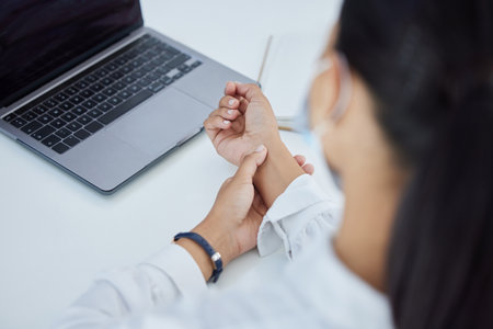 Business woman with a wrist injury, pain or accident from typing or stress sitting by a desk in her office. Girl with muscle sprain, inflammation or carpal tunnel with medical emergency at workplace.の写真素材