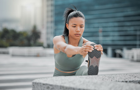 Sporty young hispanic female athlete stretching her legs before a run outside . Fit young woman warming up while exercising in the city. Exercise is good for your health and wellbeingの写真素材