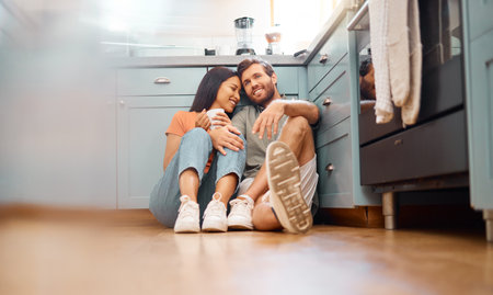 Young happy interracial couple bonding while drinking coffee together at home. Loving caucasian boyfriend and mixed race girlfriend sitting on the kitchen floor. Cheerful husband and wife relaxing anの写真素材