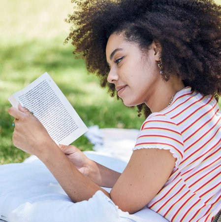 Black woman reading book, relax in park and picnic blanket with novel in nature. Education, learning and female student in Brazil in college or university campus on grass field studying with textbookの写真素材