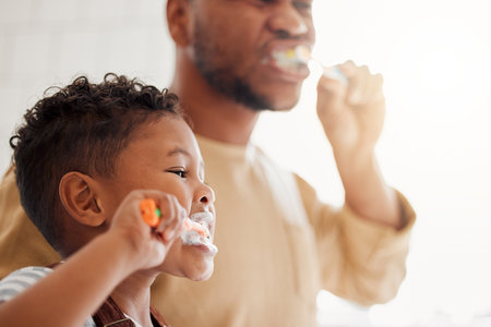 Happy mixed race father and son brushing their teeth together in a bathroom at home. Single African American parent teaching his son to protect his teethの写真素材