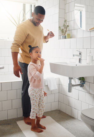 Happy mixed race father and daughter brushing their teeth together in a bathroom at home. Single African American parent teaching his daughter to protect her teethの写真素材