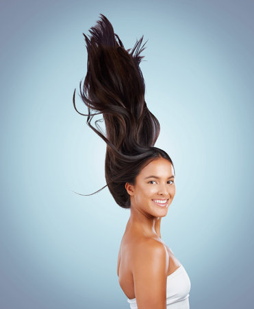 Portrait of a hispanic brunette woman with long lush beautiful hair smiling and posing against a grey studio background. Mixed race female standing showing her beautiful healthy hairの写真素材