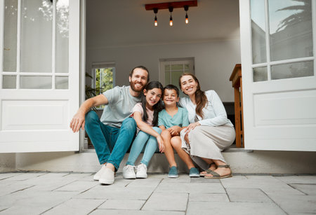 Happy young caucasian family of four sitting at their front door smiling and looking at the camera. Two parents sitting with their little son and daughter in front of their houseの写真素材