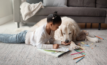 Sweet little mixed race child doing her homework while lying on the living room carpet with her puppy. Child colouring while bonding with her emotional support rescue dogの写真素材