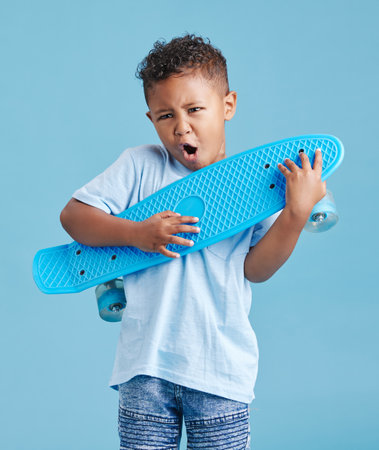 Playful kid using his skateboard as an air guitar. Adorable little mixed race boy looking excited while holding his skateboardの写真素材