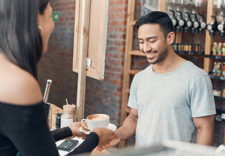 Young hispanic waiter serving a cup of coffee to a customer while working in a cafe. Friendly barista and coffeeshop owner managing a successful restaurant startupの写真素材