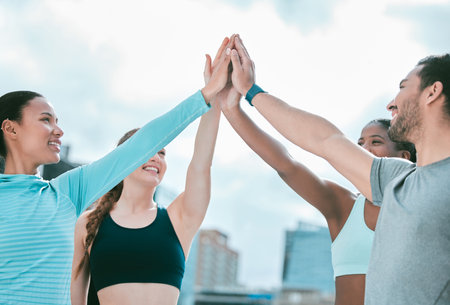 Diverse group of happy sporty people joining hands to high five for celebration of unity and support. Motivated athletes huddled for workout encouragement. Merging for collaboration, team spirit andの写真素材