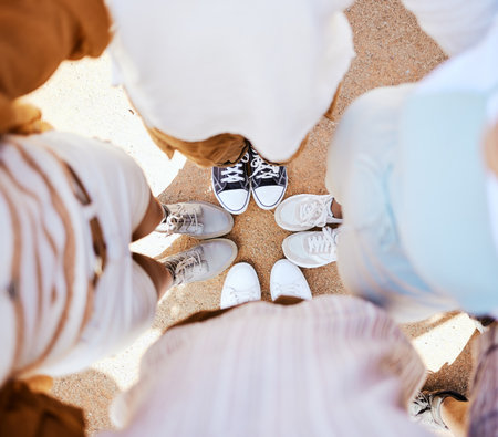 Friends, group and circle with shoes together for happiness, solidarity and bonding on holiday. People, sneakers and happy together with feet on sand in fun huddle on travel, vacation or road tripの写真素材