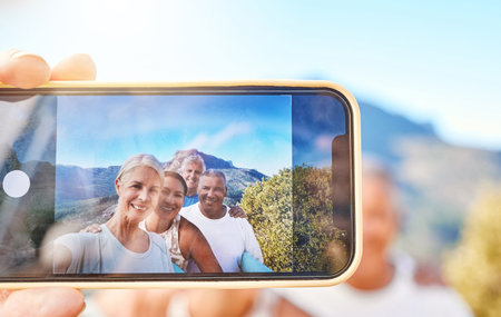 Close up of device screen while active senior people pose together for a selfie outdoors. Group of mature people exercising in natureの写真素材