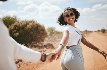 Couple, walking and nature with a black woman and man outdoor holding hands on a sand road in a dessert together. Travel, love and romance with a female and male on a date during summer vacationの写真素材