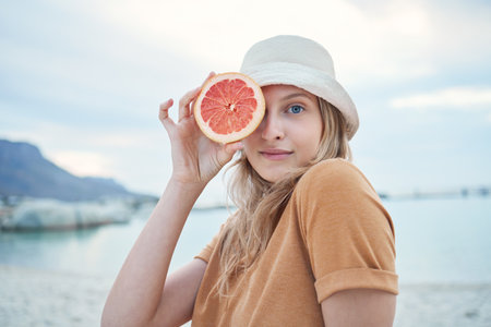Grapefruit, wellness and woman on tropical beach for nature holiday, vacation or outdoor vitamin c health. Vegan, youth lifestyle for skin care, detox or healthy eating with sky mockup and sea waterの写真素材