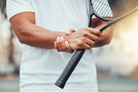 Closeup of unknown indian tennis player suffering from wrist injury in court game. Ethnic fit professional in pain while holding and rubbing hand after match. Sporty man holding racket in sports clubの写真素材