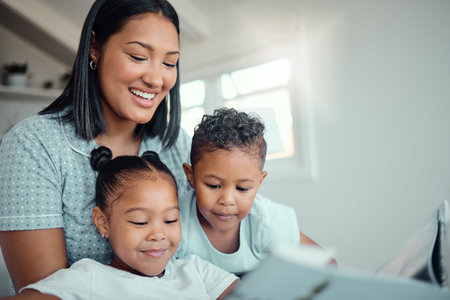 Young mixed race mother reading a storybook while relaxing at home with her two children. Smiling...