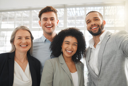 Portrait of a group of four cheerful diverse and positive businesspeople taking a selfie together at work. Happy mixed race businessman taking a photo with his joyful colleaguesの写真素材