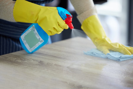Hands, gloves and spray cleaning table with disinfectant for clean house. Kitchen counter, home safety and disinfection with alcohol solution in bottle to protect home from germs, dust and bacteria.の写真素材