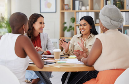 Diverse group of smiling business women having a brainstorm meeting in office. Happy confident professional team sitting together and using paperwork while talking and planning a marketing strategyの写真素材