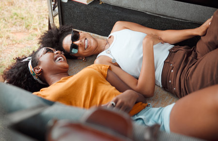 Camper, relax and friends laughing and bonding on road trip, lying in a campervan and talking. Travel, freedom and women in nature, happy while chilling in vehicle and enjoying carefree conversationの写真素材