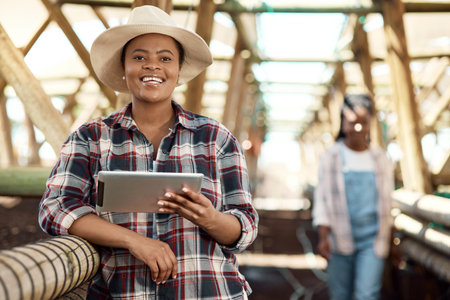 Happy farmer using a digital tablet. African american farmer using a digital device. Portrait of a smiling farmer standing in a greenhouse. farm worker holding wireless tech device.の写真素材